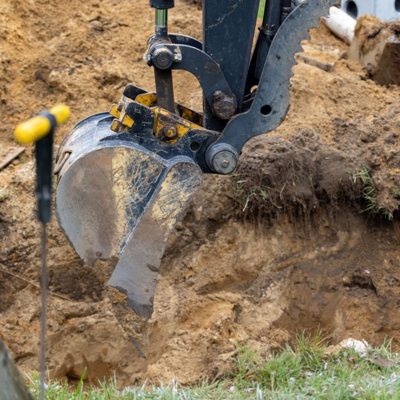 Close-up of an excavator bucket digging into brown soil at a construction site.