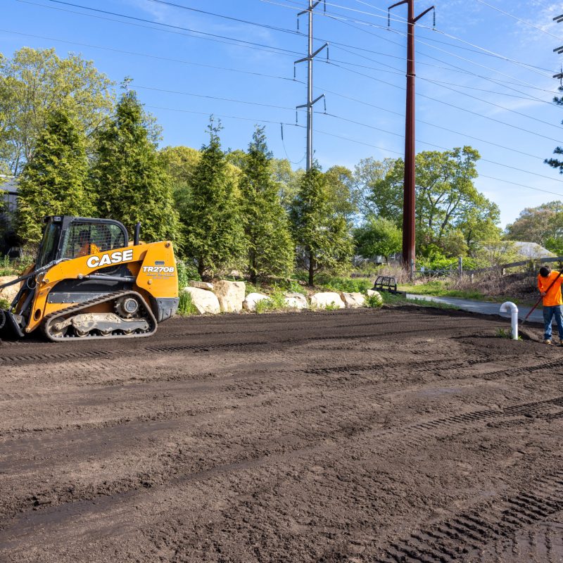 Yellow CASE skid steer parked on a dirt construction site with a worker in an orange safety shirt nearby.